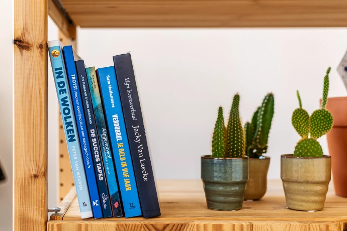 Boeken die Hans schreef in ghostwriting staan in houten boekenkast met cactussen